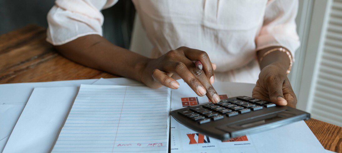 Foto que ilustra matéria sobre portabilidade de crédito imobiliário, com uma pessoa com camisa social clara usando uma calculadora.