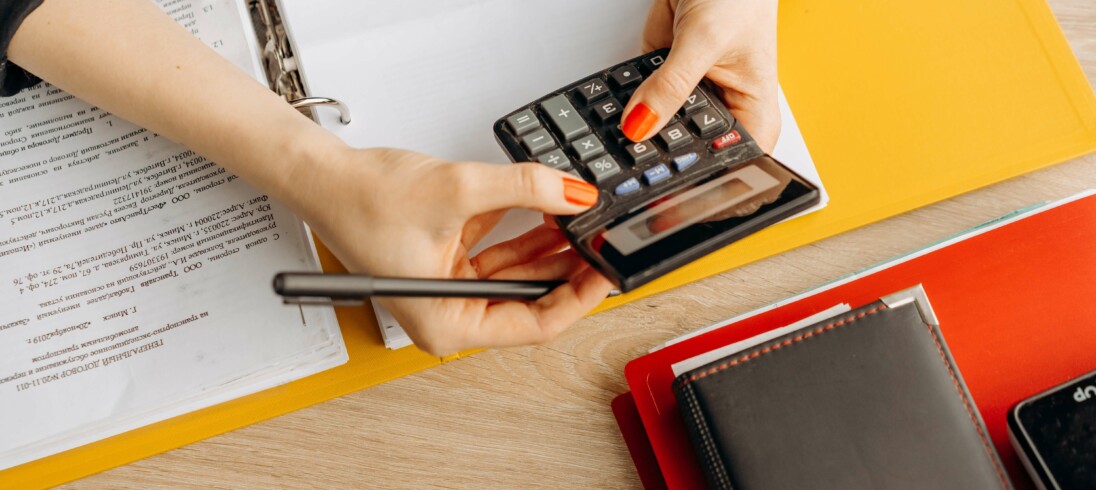 Foto que ilustra matéria sobre financiar imóvel, com as mãos de uma mulher fazendo contas em uma calculadora.