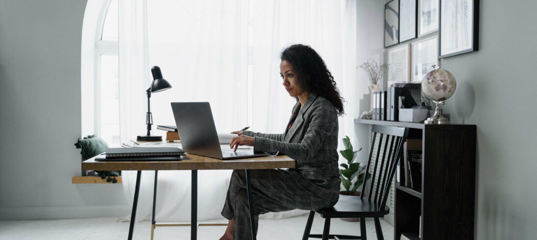 Foto que ilustra matéria sobre investir em imóveis, com uma mulher sentada em frente a um computador fazendo uma pesquisa.
