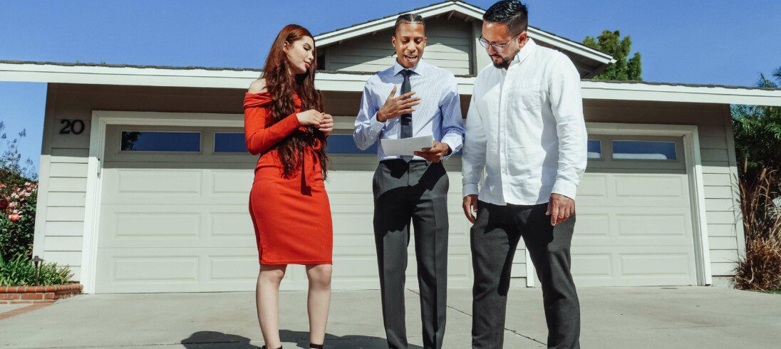 Foto que ilustra matéria sobre fiador de aluguel com dois homens e uma mulher em frente a uma casa, onde um homem está segurando um contrato.