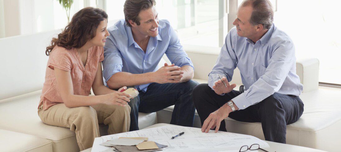 Em matéria sobre valorização de imóvel, casal conversa com consultor imobiliário. Os três estão sentados em um sofá, com uma papelada sobre uma mesa de centro.