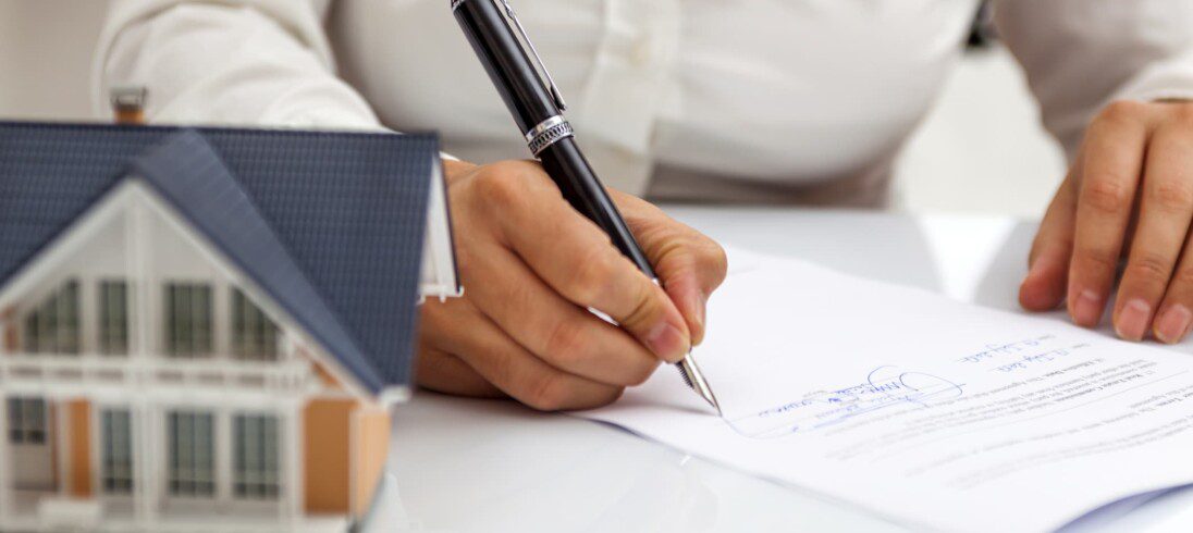 imagem em close de uma mulher assinando documentos de compra ilustrando artigo sobre imóvel com dívida de condomínio