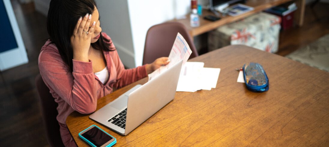 foto de mulher sentada diante de uma mesa de madeira analisando um notebook e papéis ilustrando artigo sobre como declarar imóvel financiado no imposto de renda