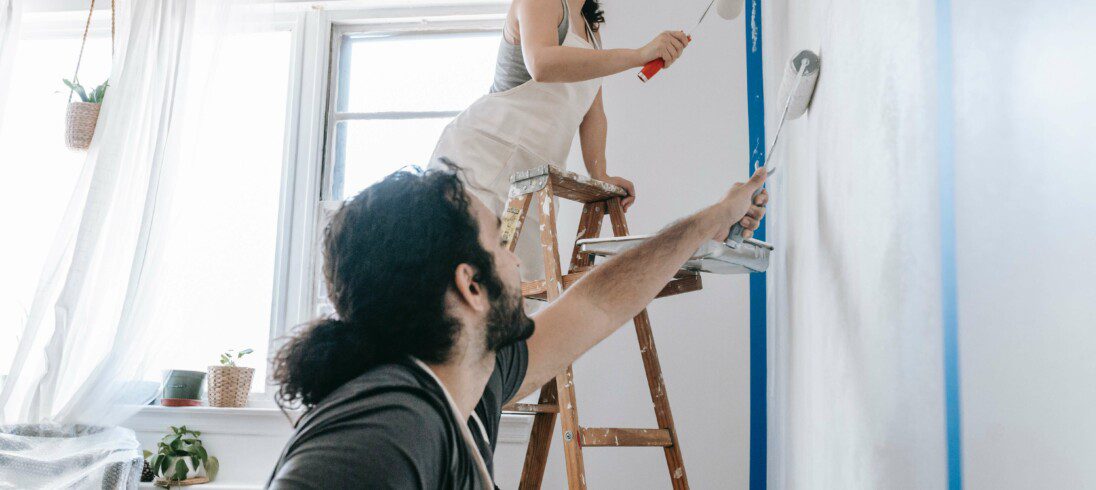Foto que ilustra matéria sobre reforma em apartamento, com uma mulher passando um rolo de tinta em uma parede.