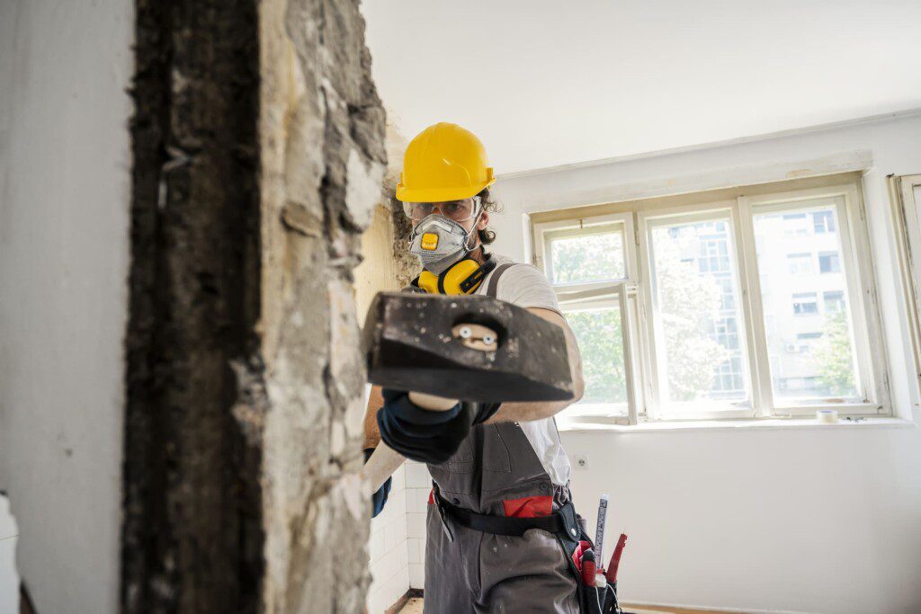 Trabalhador usando martelo durante a reforma de um apartamento. Imagem disponível em Getty Images.