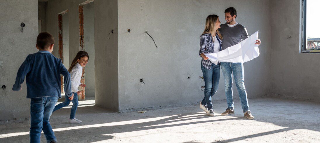 Família feliz analisando planos em seu novo apartamento, em reforma. Imagem disponível em Getty Images.