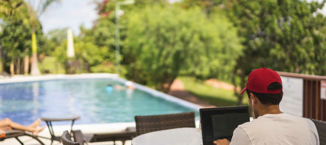 Homem usando computador sentado diante de uma piscina