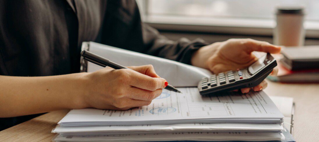 Foto que ilustra matéria sobre refinanciamento imobiliário, com uma mulher segurando uma caneta e uma calculadora, fazendo anotações.