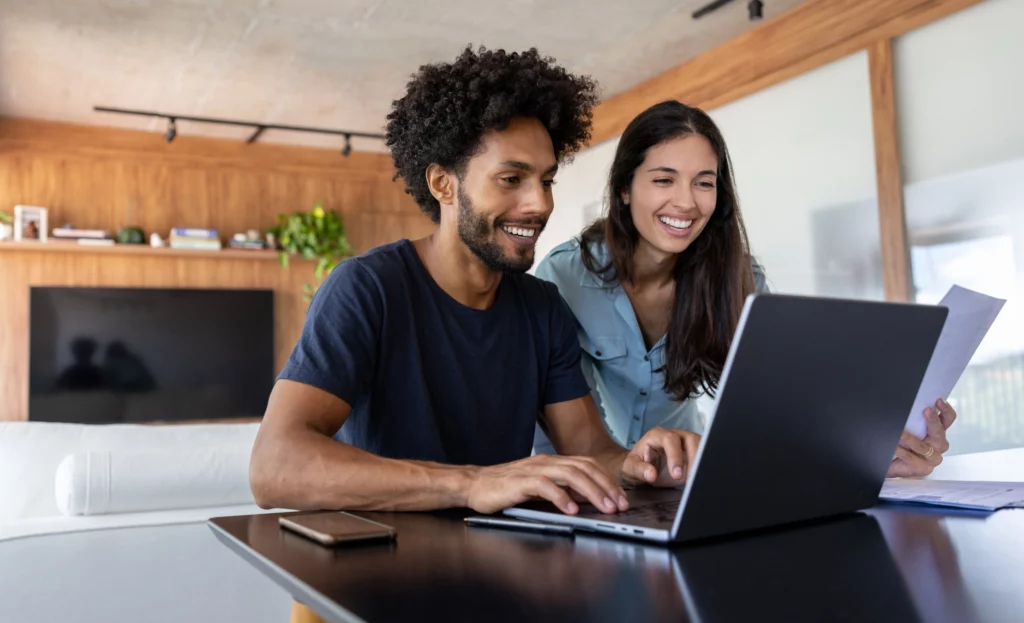 Imagem de um casal composto por um homem e uma mulher em frente a um computador que está em cima da mesa de uma casa para ilustrar matéria sobre o que é seguro fiança