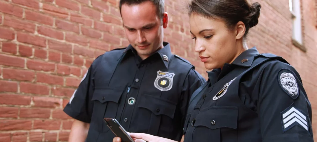 Foto que ilustra matéria sobre programa habitacional para agentes de segurança, o Habite Seguro, mostra um policial homem e uma policial mulher olhando para um celular.