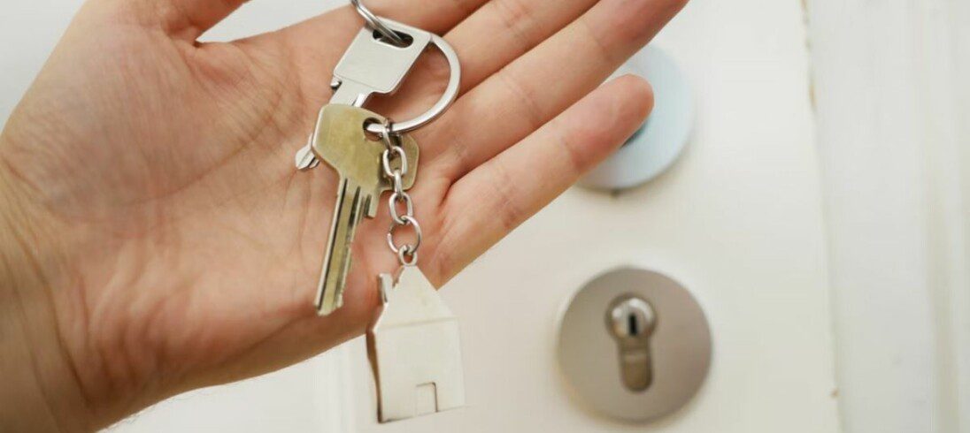 mão segurando um chaveiro com chaves em frente a uma porta