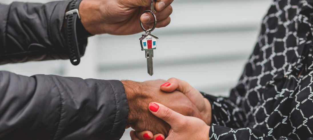 Imagem mostra mão masculina e feminina apertando, e uma das mãos segura uma chave de casa. Imagem disponível no Pexels