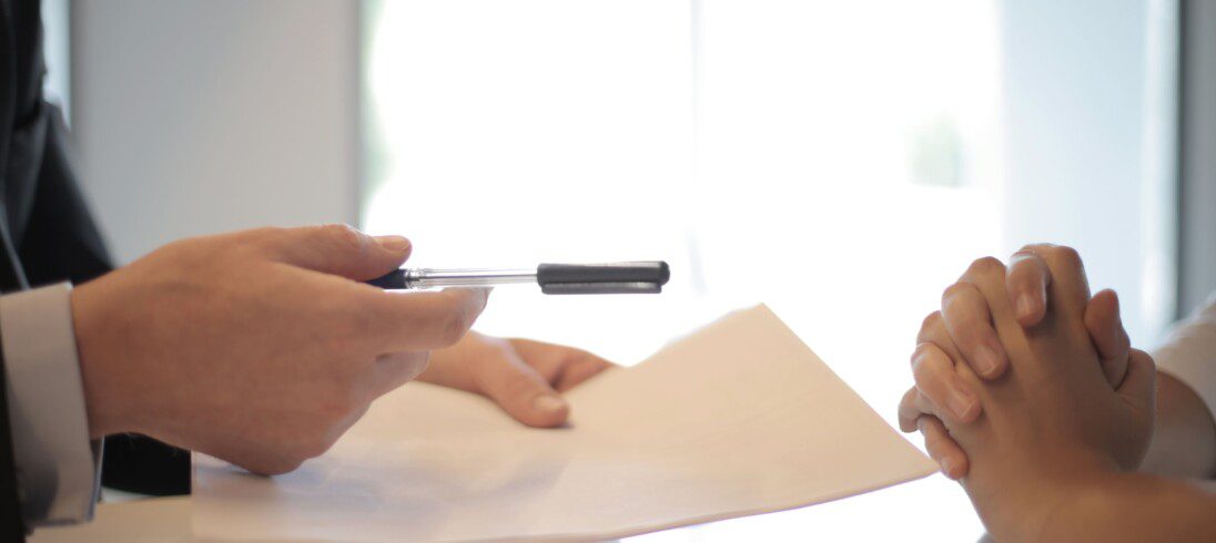 Pessoas assinam contrato com uma caneta preta.