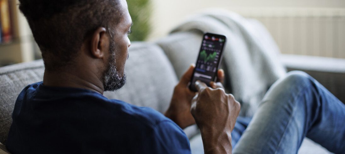 Foto que ilustra matéria sobre como fatores políticos influenciam o mercado imobiliário mostra um homem negro de costas olhando para seus investimentos no celular.