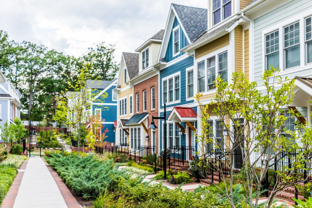 A imagem mostra um conjunto de casas coloridas. Cada casa é de uma cor: azul, amarelo, branco, laranja. Em frente a cada uma há um jardim.