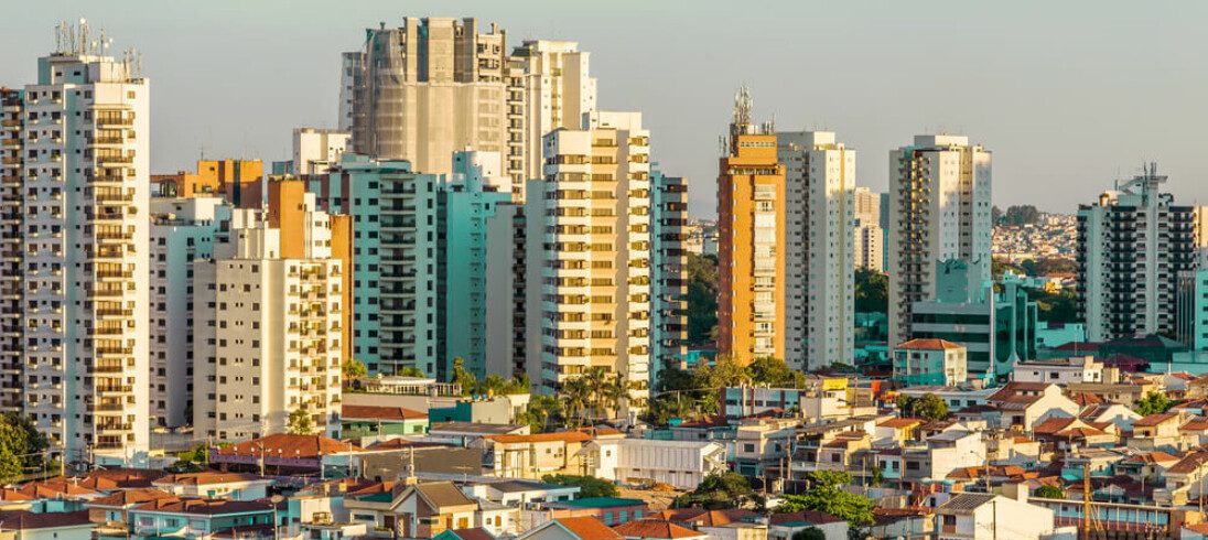 Foto que ilustra matéria sobre tipos de moradia mostra uma parte da cidade de São Paulo com muitas casas em primeiro plano e prédios altos ao fundo.