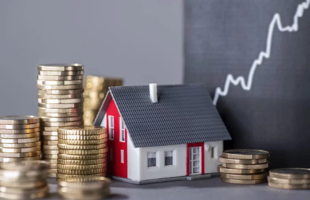 Imagem de uma casa em miniatura ao lado de algumas moedas empilhadas para ilustrar matéria sobre o que significa taxa referencial