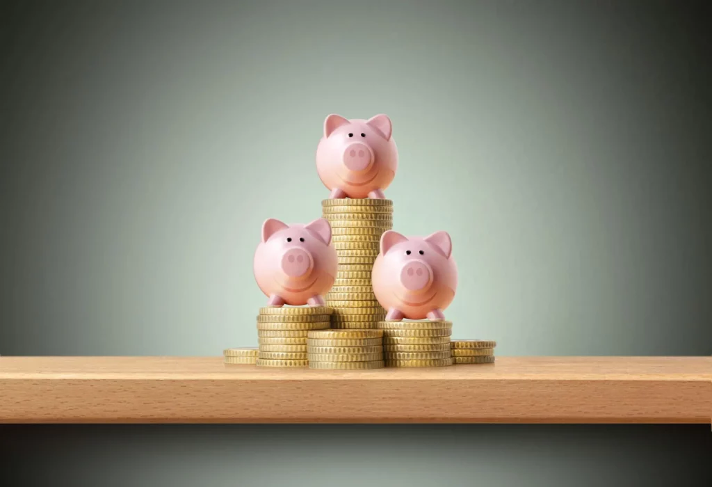 Imagem de três figuras de porquinhos empilhados em cima de moedas douradas para ilustrar matéria sobre qual o valor da taxa referencial hoje