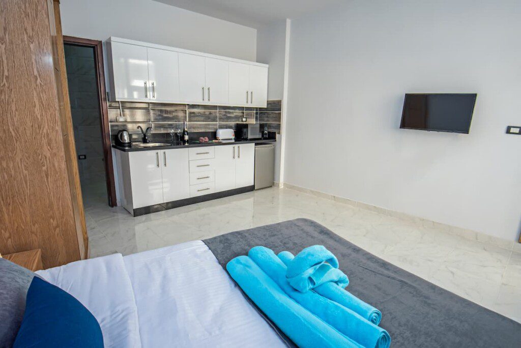 Kitnet com cama, armários de cozinha e televisão.