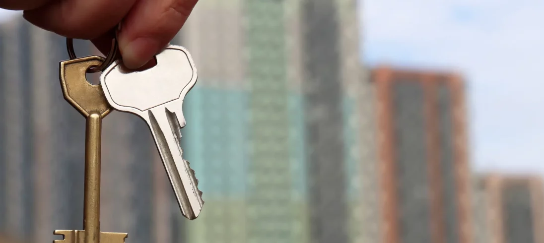 Foto de alguém segurando uma chave na frente de um condomínio.