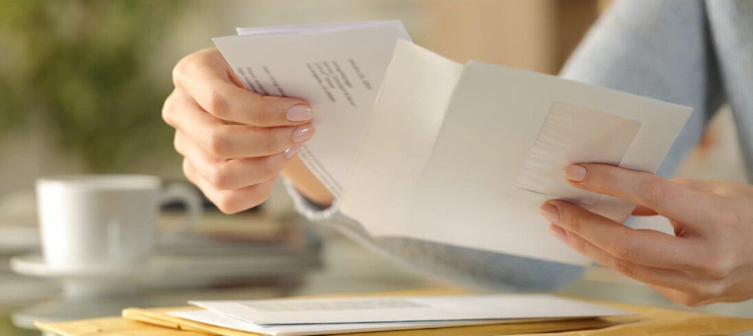 Mãos com características femininas abrem um envelope de carta.