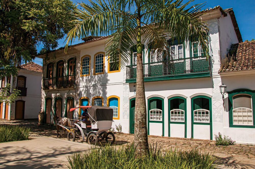 Foto que ilustra matéria sobre sobrado mostra casas coloniais brancas com os batentes de portas em diferentes cores, como verde e amarelo. 