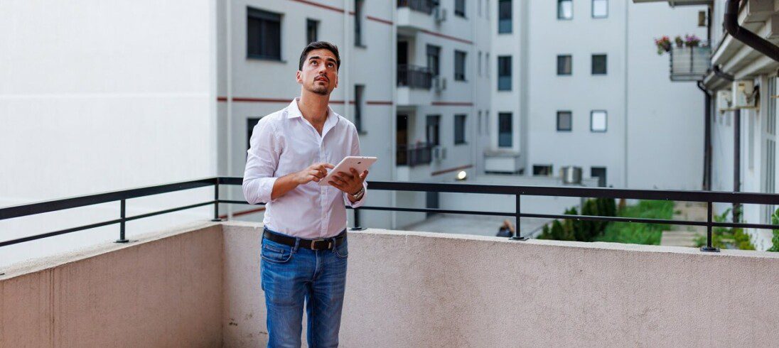 Foto que ilustra matéria sobre síndico profissional mostra um homem na varanda de um apartamento olhando para cima e verificando algo no prédio.