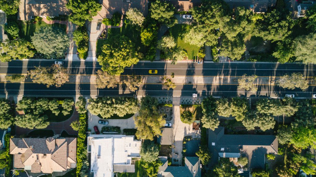 Imagem aérea de um bairro residencial arborizado com vista para a parte de cima das casas e carros das residências