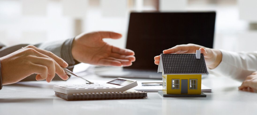Foto que ilustre matéria sobre taxa de juros crédito imobiliário mostra duas pessoas com uma mesa ao centro e papéis na mesa com uma calculadora