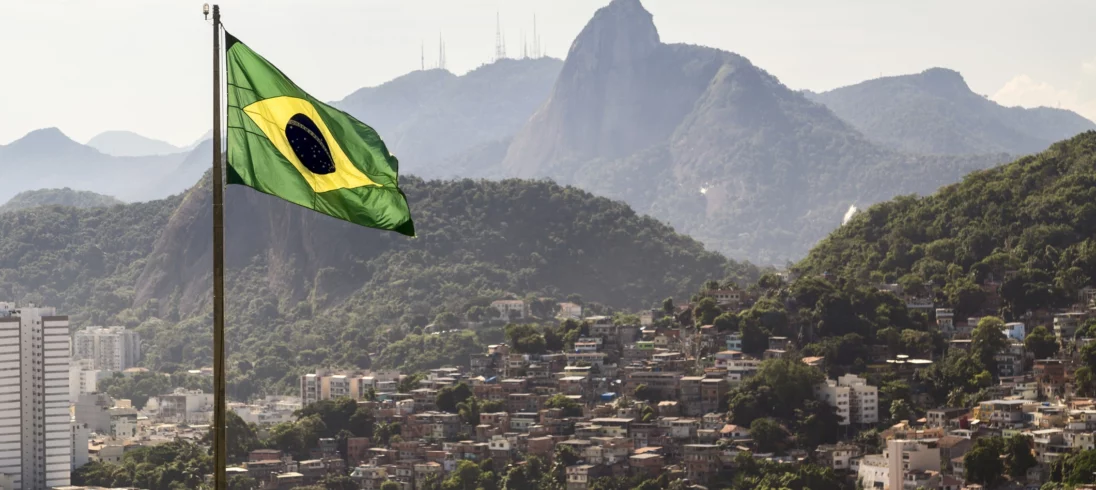 Imagem de uma bandeira brasileira na frente do Corcovado e vários prédios da região para ilustrar matéria sobre o IDH dos estados brasileiros