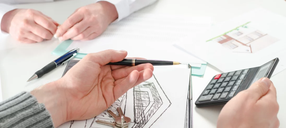 Imagem de uma pessoa segurando uma calculadora e uma caneta enquanto outra pessoa observa para ilustrar matéria sobre qual a entrada ideal para comprar um imóvel