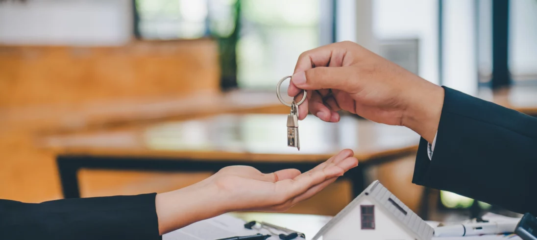 Imagem de duas pessoas finalizando um contrato imobiliário, onde uma delas entrega uma chave para a outra pessoa para ilustrar matéria sobre entrega de chaves