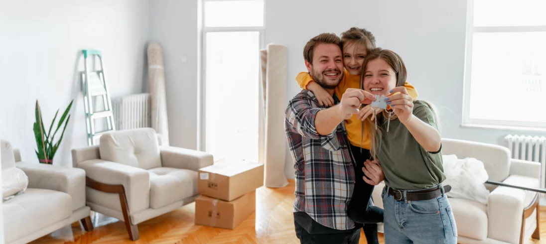 Imagem de um casal composto por um homem e uma mulher, ao lado de uma criança, segurando a chave da nova casa para ilustrar matéria sobre melhor época para alugar apartamento