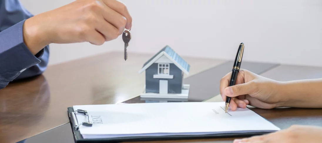 Imagem de uma mão segurando uma chave enquanto outra pessoa assina um documento para ilustrar matéria sobre o que impede o registro de um imóvel