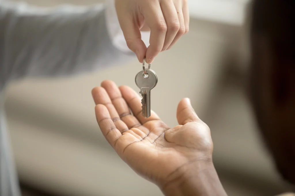 Uma pessoa com a mão estendida com a palma para cima segurando uma chave para representar o termo de entrega de chaves