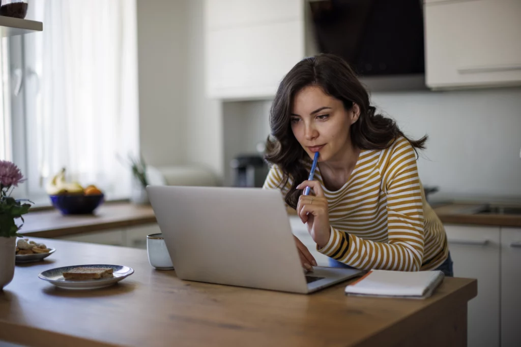Imagem de uma mulher na cozinha de uma casa em frente a um computador para ilustrar matéria sobre se todo empréstimo consignado tem seguro prestamista