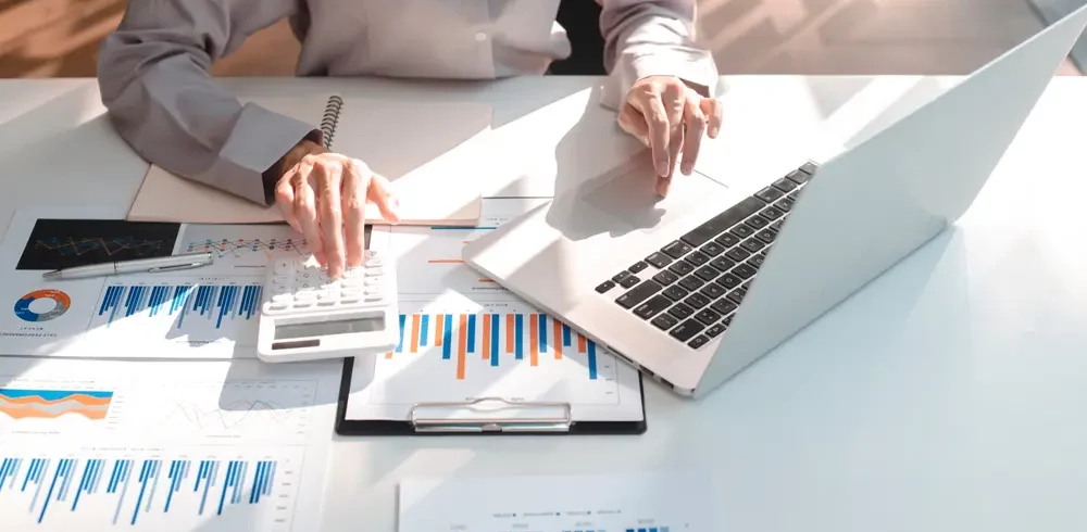 Foto que ilustra matéria sobre IVAR x IGP-M mostra as mãos de uma pessoa em detalhe sobre uma mesa manuseando um notebook e uma calculadora sobre papeis com diversos gráficos (Foto: Shutterstock)
