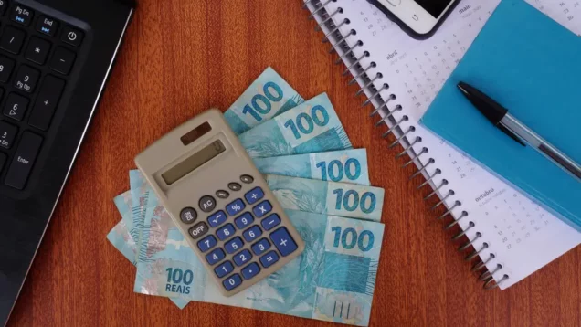 Foto que ilustra matéria com números na tabela IGP-M mostra uma calculadora em cima de algumas notas de 100 reais e ao lado de um calendário, um bloquinho, uma caneta, um celular e um notebook (Foto: Shutterstock)