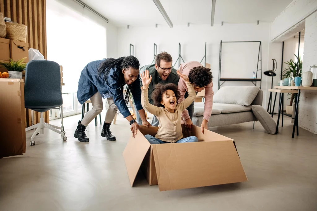 Imagem de uma família brincando em casa com as crianças e uma caixa de papelão para ilustrar matéria sobre como escolher tamanho de apartamento