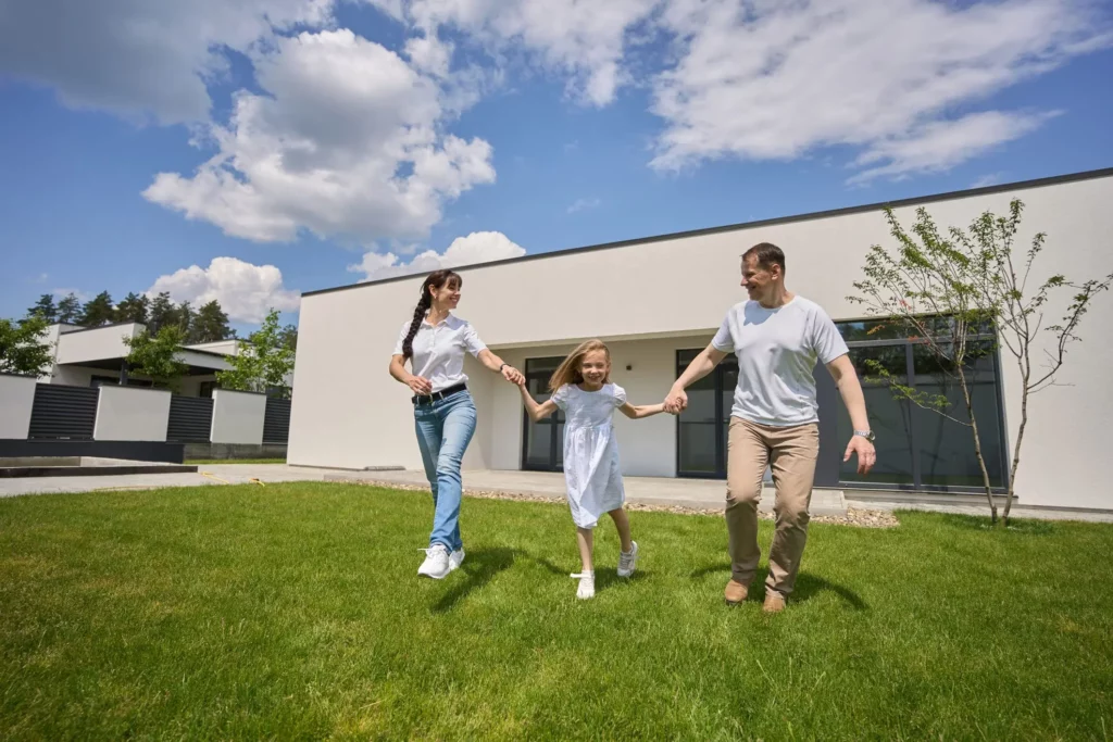 Imagem de uma família composta por um homem, uma mulher e uma criança de mãos dadas correndo no gramado de uma casa para ilustrar matéria sobre construir em loteamento fechado