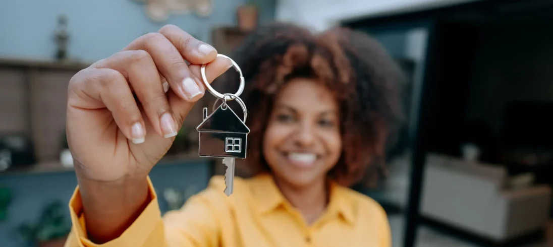Imagem de uma mulher com blusa amarela segurando uma chave com chaveiro de casa para ilustrar matéria sobre qual score ideal para financiamento de imóvel