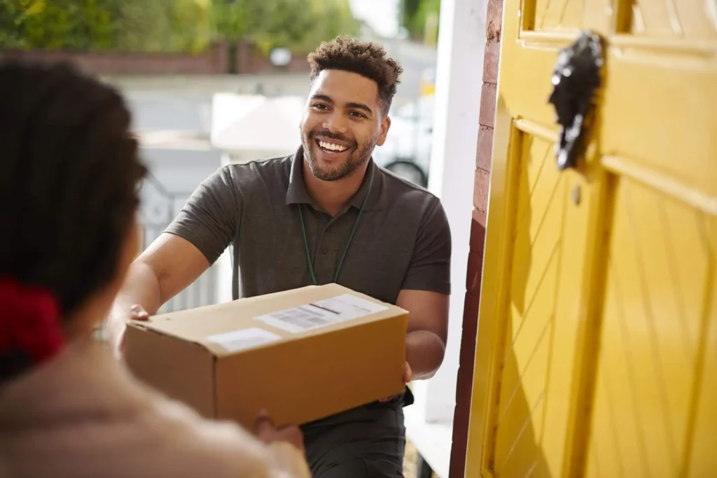 Imagem de um homem entregando uma encomenda dentro de uma caixa na porta da casa de uma mulher para ilustrar matéria sobre o que é o código de endereçamento postal
