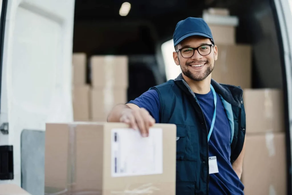 Imagem de um homem na frente de uma van de entregas segurando uma caixa de papelão com um sorriso no rosto para ilustrar matéria sobre como descobrir meu código postal
