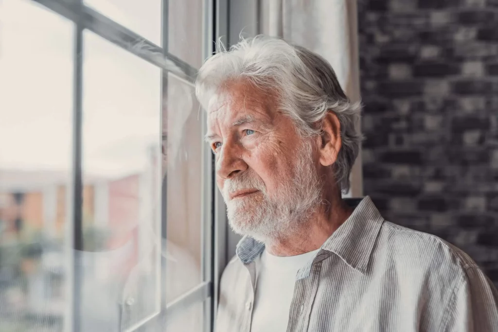 Imagem  de um idoso com cabelos brancos olhando pensativo para uma janela para ilustrar a matéria sobre herdeiro de imóvel de falecido 