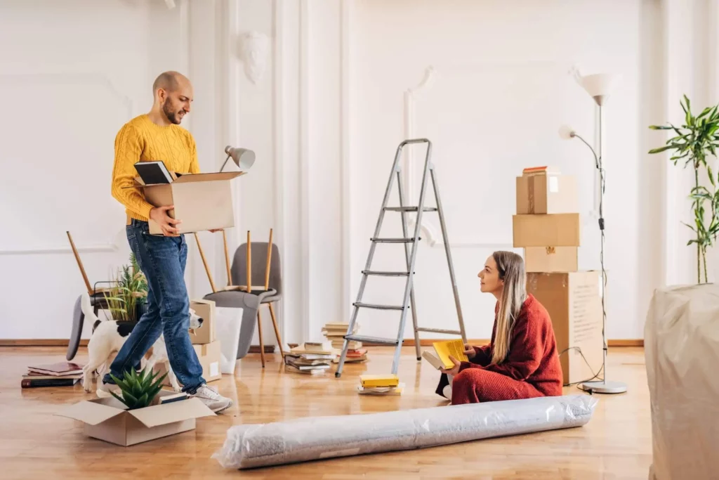 Imagem de um casal composto por um homem e uma mulher fazendo alguma obra em casa e carregando caixas de papelão para ilustrar matéria sobre a HIS, habitação de interesse social
