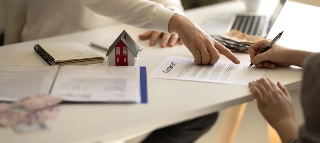 Imagem de uma pessoa assinando um contrato de aluguel enquanto outra pessoa aponta para o documento para ilustrar a matéria sobre modelo de contrato de locação
