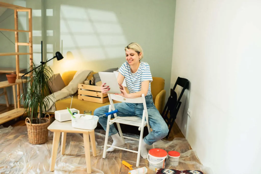 Imagem de uma mulher sentada em uma cadeira de metal branca na sala de uma casa para ilustrar matéria sobre o que é habitação de interesse social