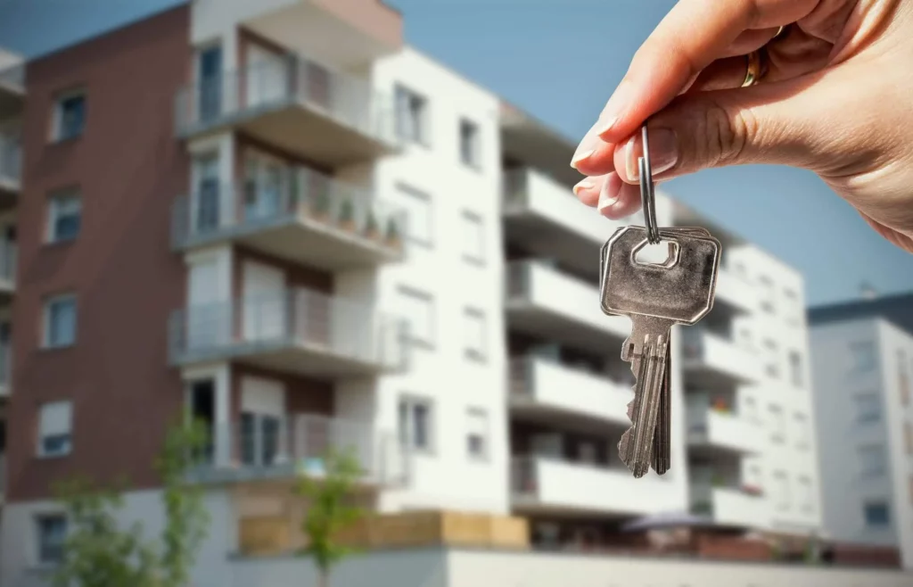 Imagem de uma pessoa segurando uma chave de uma casa com um prédio ao fundo para ilustrar matéria sobre como mudar titularidade do iPTU para meu nome