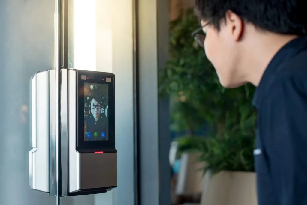 Imagem um homem asiático usando a biometria facial para destravar a porta de vidro em um prédio para ilustrar matéria sobre as características de um condomínio conectado com tecnologia