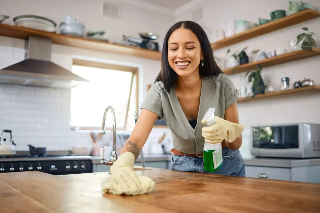 Imagem de uma mulher com luvas limpando a bancada de uma cozinha com um produto de limpeza para ilustrar matéria sobre cuidados com imóvel alugado